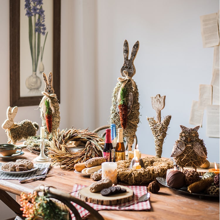 A collection of rustic Christmas figurine decorations including a hen, owl, rabbit, and flowers, crafted from natural wood and straw.