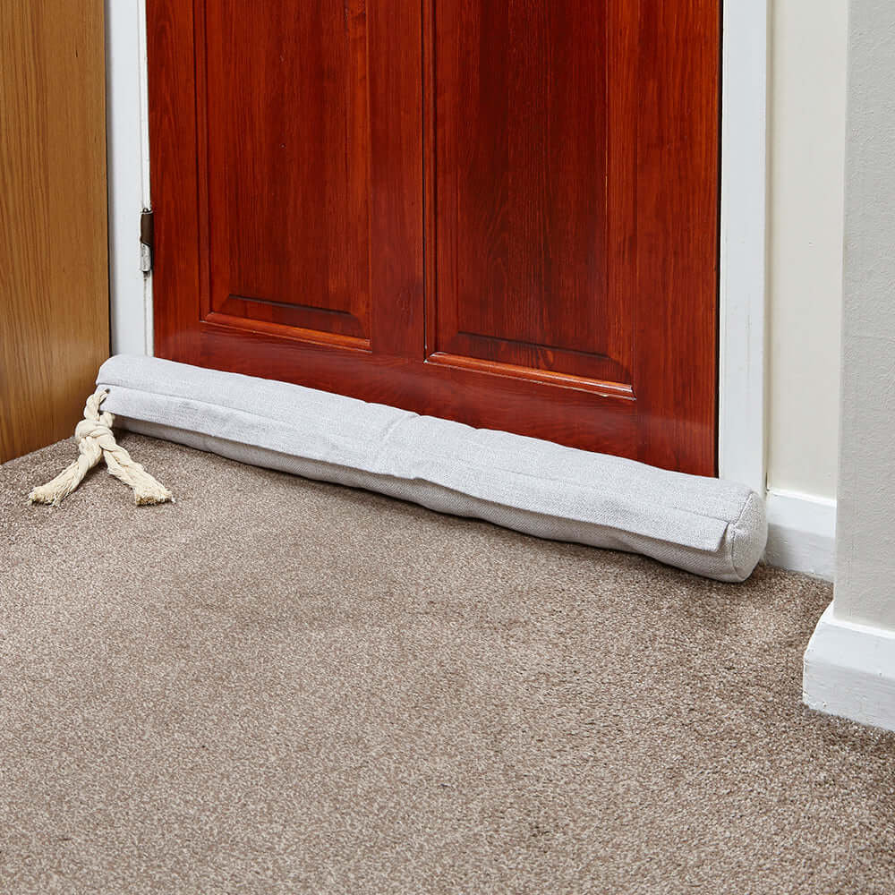 Cream door draught excluder placed at the bottom of a door, effectively blocking drafts and enhancing home comfort.