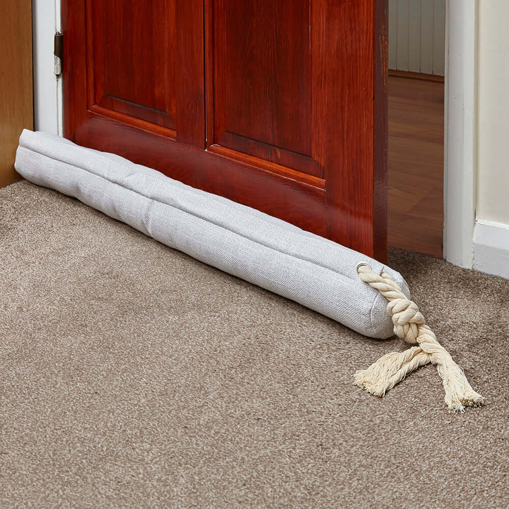 Cream door draught excluder placed at the bottom of a door, effectively blocking drafts and enhancing home comfort.