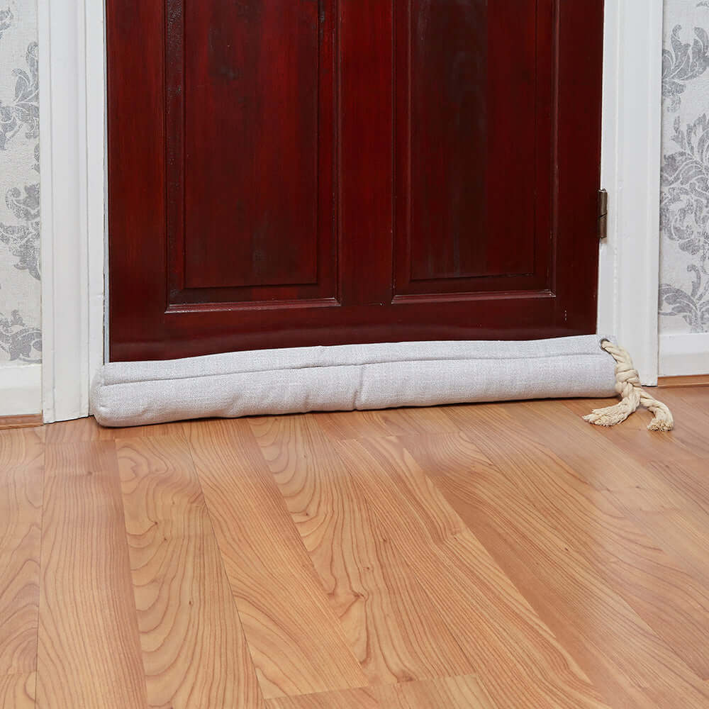 Cream door draught excluder placed at the bottom of a door, effectively blocking drafts and enhancing home comfort.