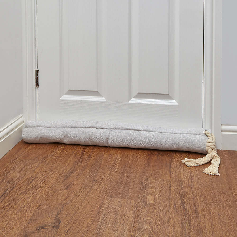 Cream door draught excluder placed at the bottom of a door, effectively blocking drafts and enhancing home comfort.