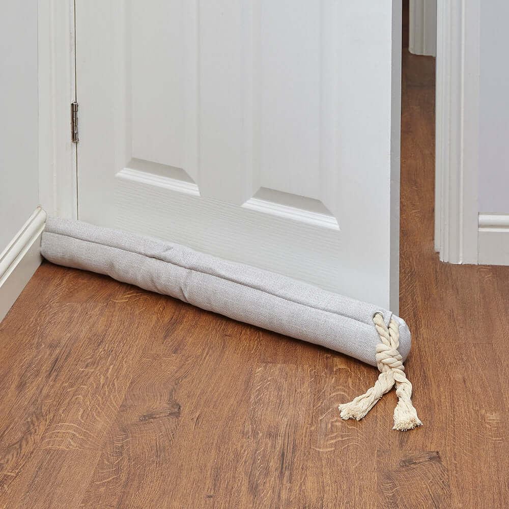 Cream door draught excluder placed at the bottom of a door, effectively blocking drafts and enhancing home comfort.