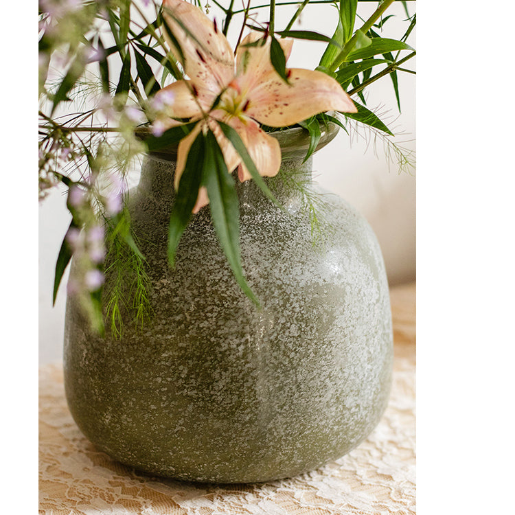 A dark green matte textured glass vase, hand-blown with a unique shape and finish, perfect for home decor.