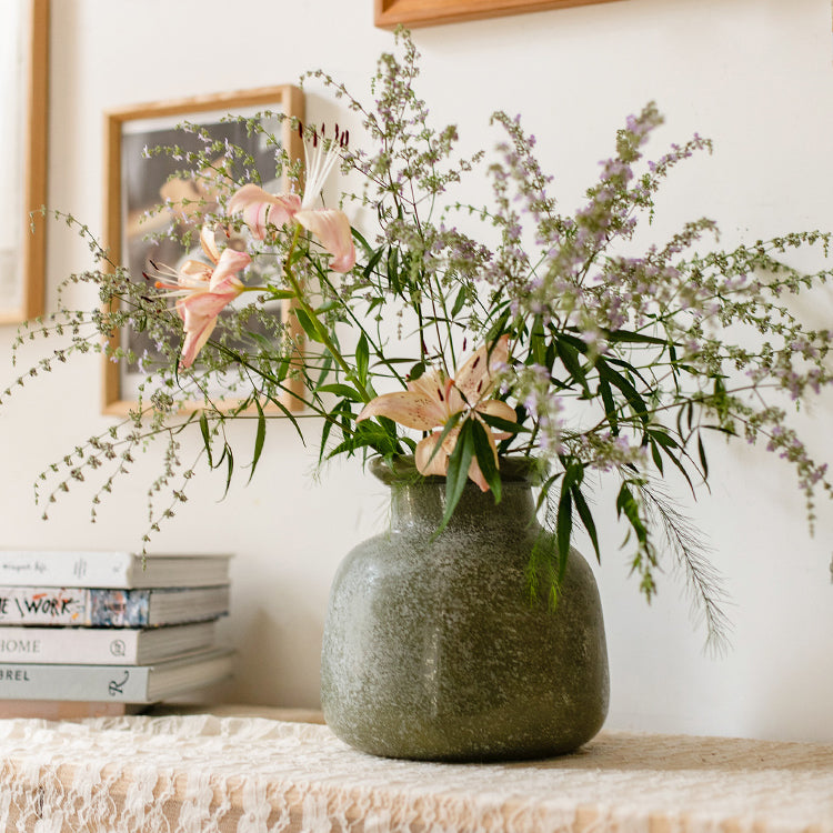 A dark green matte textured glass vase, hand-blown with a unique shape and finish, perfect for home decor.