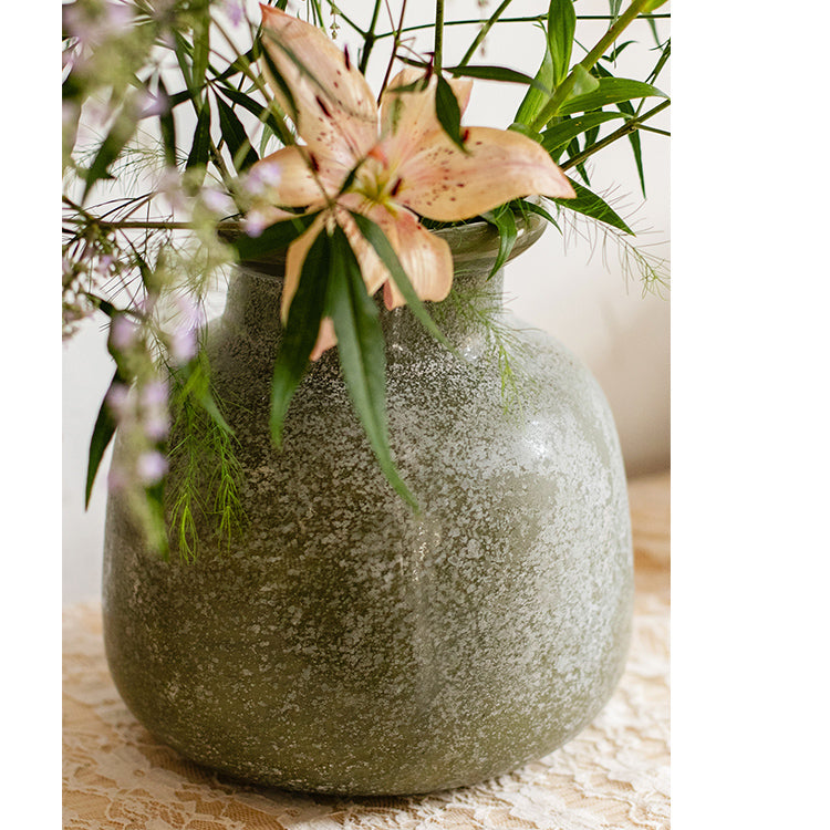 A dark green matte textured glass vase, hand-blown with a unique shape and finish, perfect for home decor.