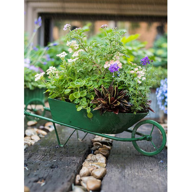 Decorative green metal planter cart showcasing plants, featuring wheels for easy mobility.