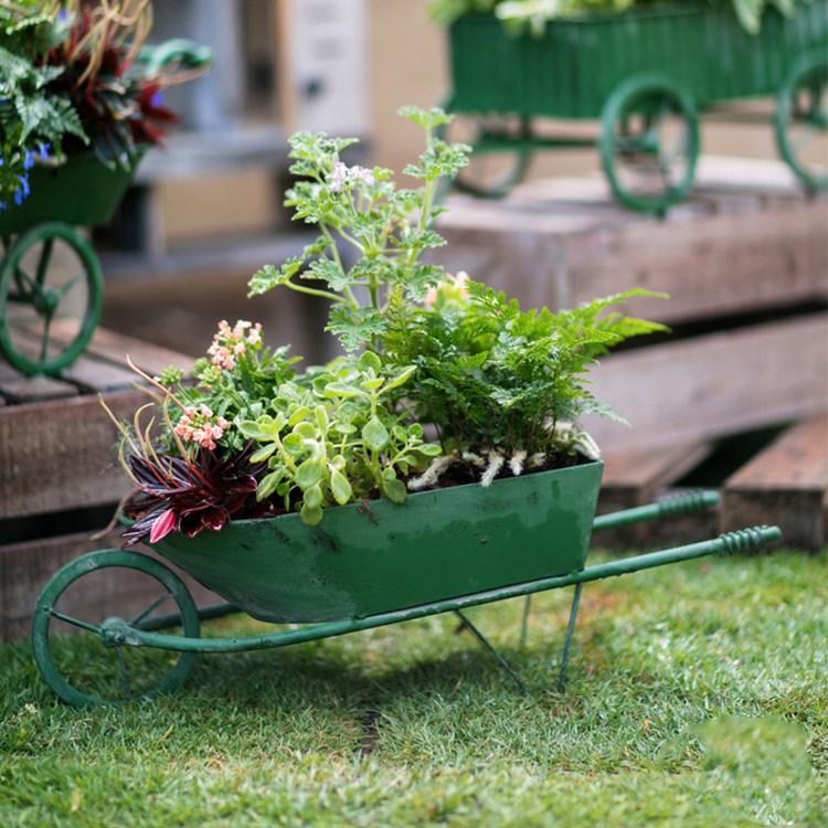 Decorative green metal planter cart showcasing plants, featuring wheels for easy mobility.