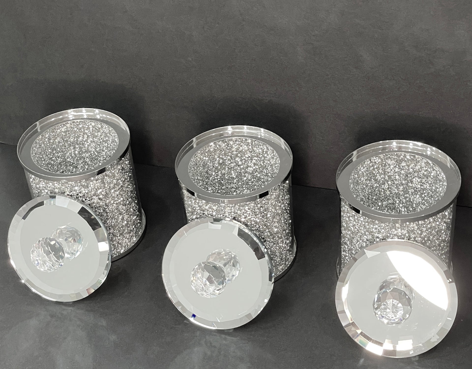 Exquisite three glass canister set with silver crushed diamond finish, featuring decorative chrome base and glass lids with handles.