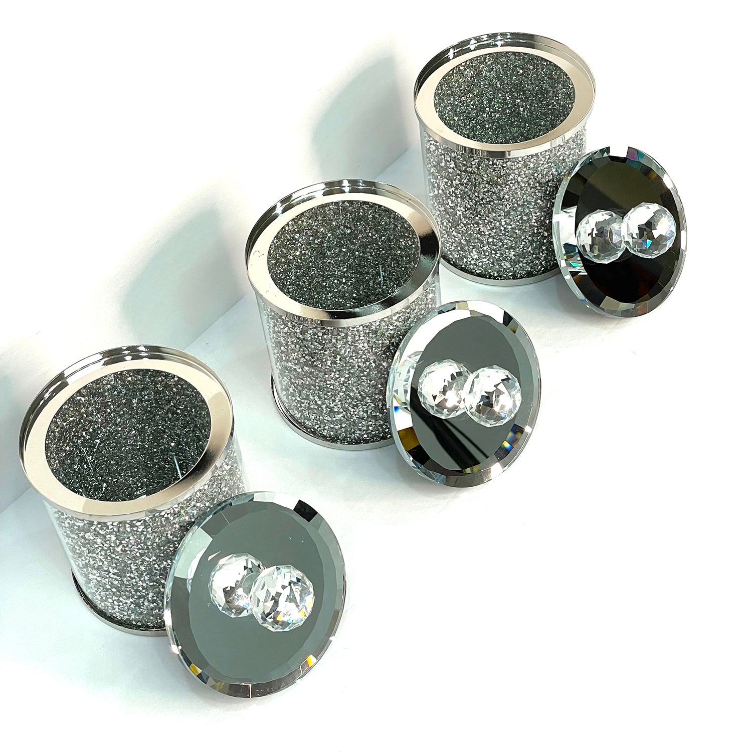 Exquisite three glass canister set with silver crushed diamond finish, featuring decorative chrome base and glass lids with handles.