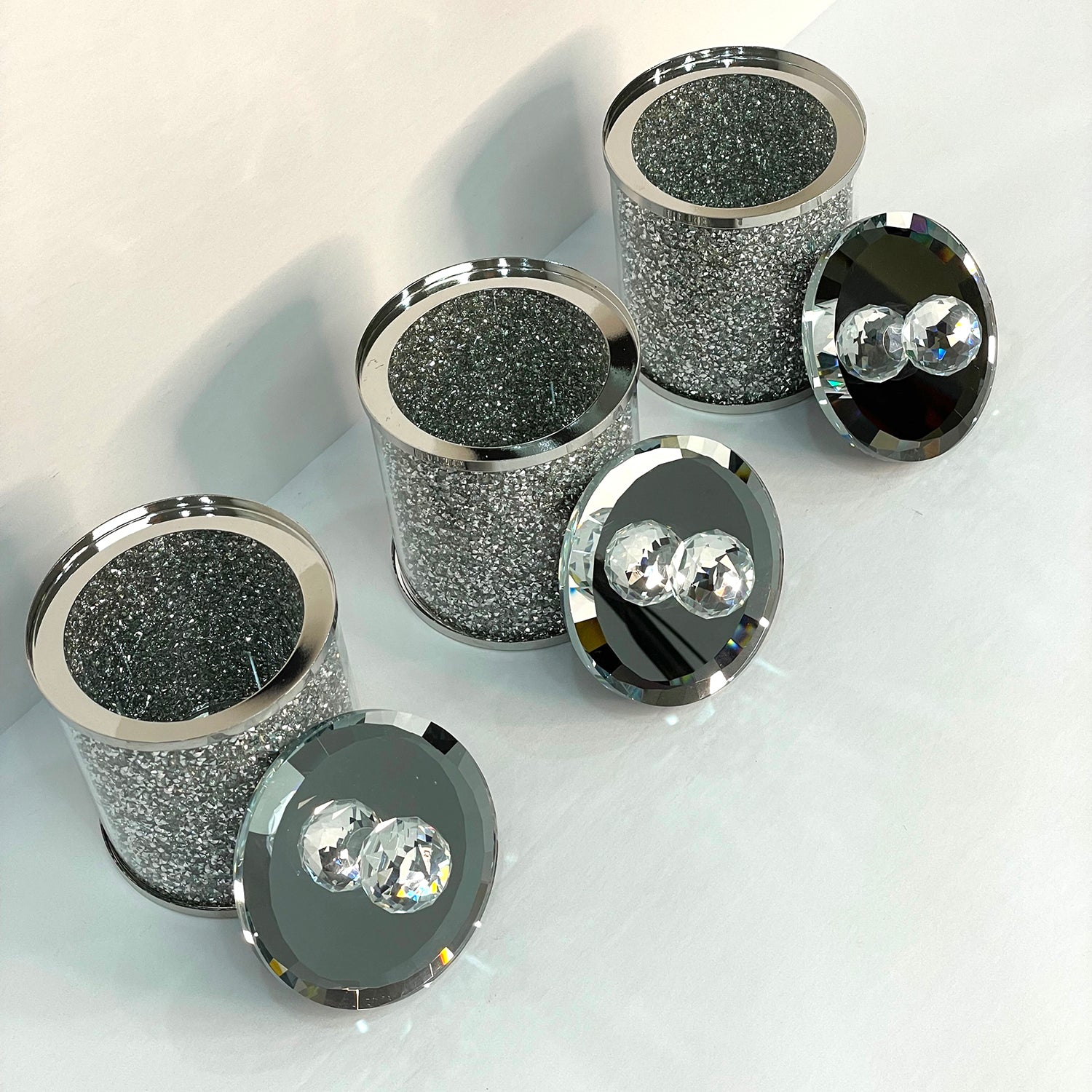 Exquisite three glass canister set with silver crushed diamond finish, featuring decorative chrome base and glass lids with handles.