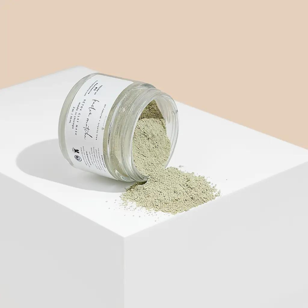 A jar of Matcha Green Facial Mask with a smooth green texture, surrounded by matcha powder and clay ingredients.