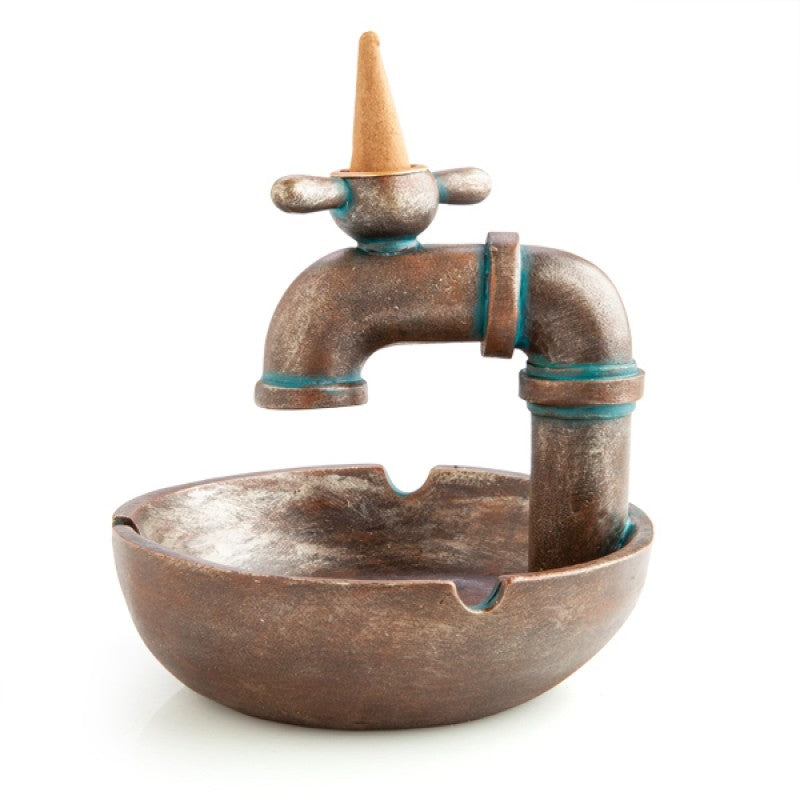 A bronze-look faucet-shaped incense burner with smoke flowing from the tap, featuring notches for resting cigarettes.