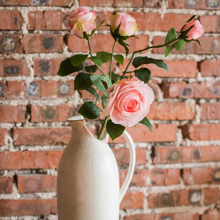 A beautiful arrangement of four light pink faux silk rose blooms on a 31-inch tall stem, showcasing realistic petals and vibrant color.