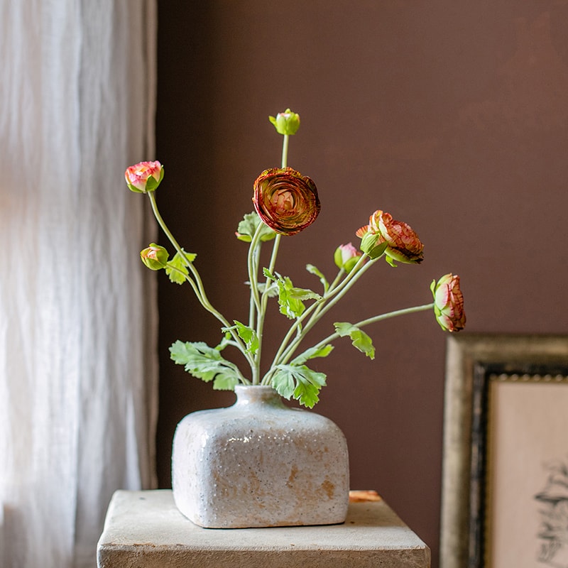 A vibrant orange Faux Silk Artificial Buttercup Flower Bundle with three stems and nine blooms, showcasing lush green leaves.