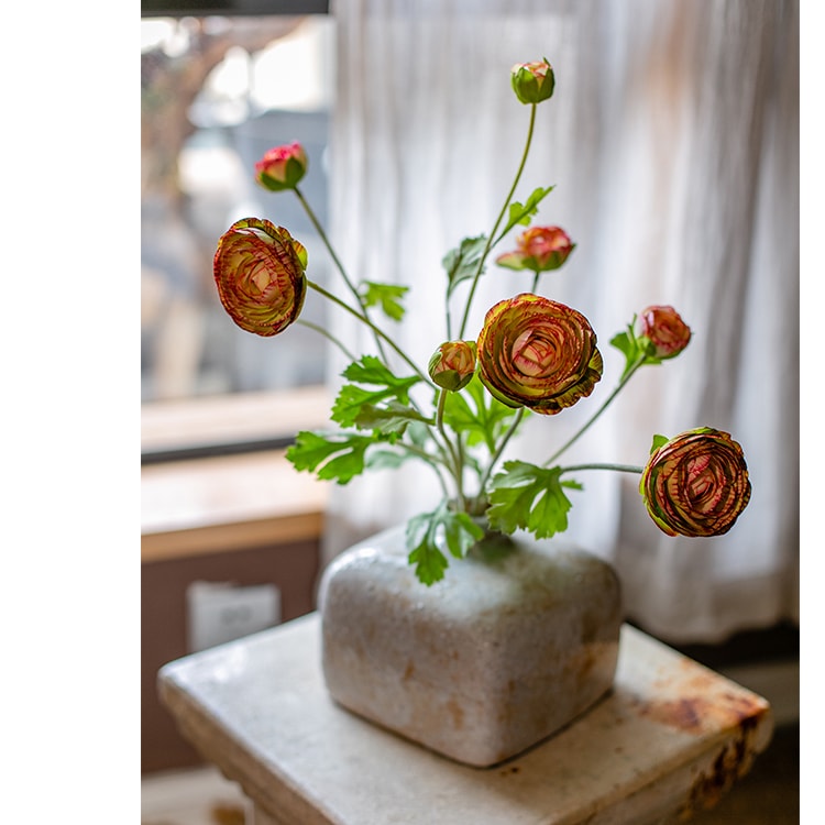 A vibrant orange Faux Silk Artificial Buttercup Flower Bundle with three stems and nine blooms, showcasing lush green leaves.