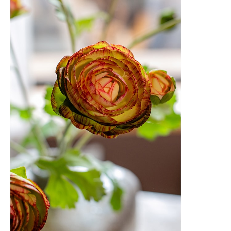 A vibrant orange Faux Silk Artificial Buttercup Flower Bundle with three stems and nine blooms, showcasing lush green leaves.