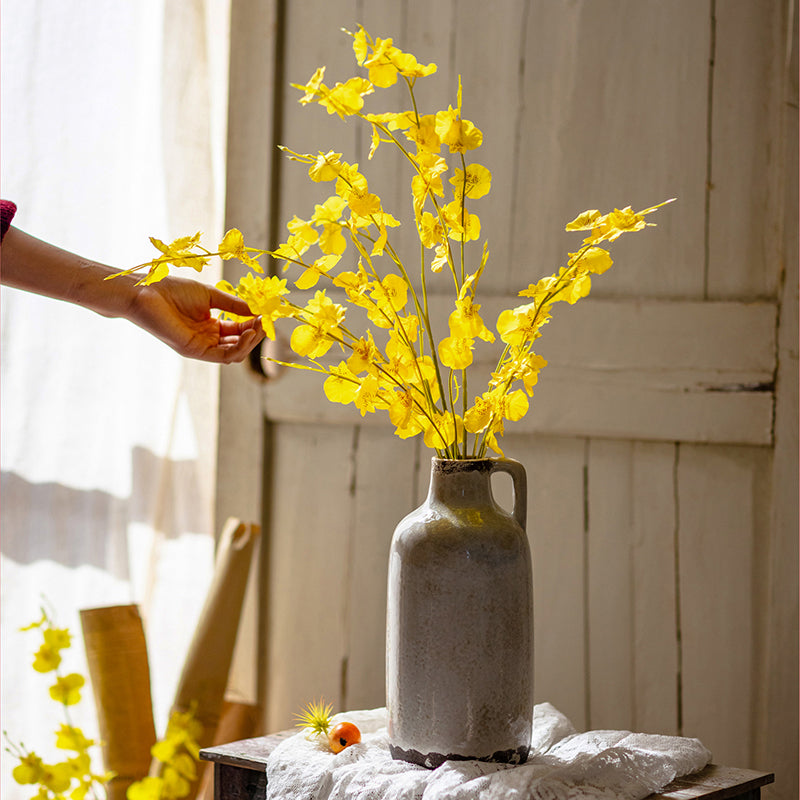 A vibrant yellow faux silk artificial Dancing Lady Orchid stem, 19 inches tall, showcasing realistic petals and leaves.