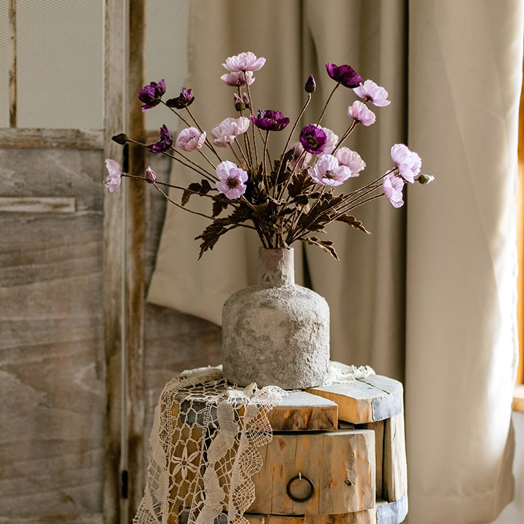 A 23-inch tall faux silk rustic poppy flower stem in purple with three blooms and one bud, featuring green leaves.