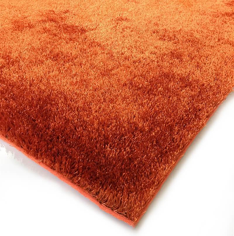 A soft shaggy rust-colored area rug, hand tufted with a cotton backing, displayed in a cozy living room setting.