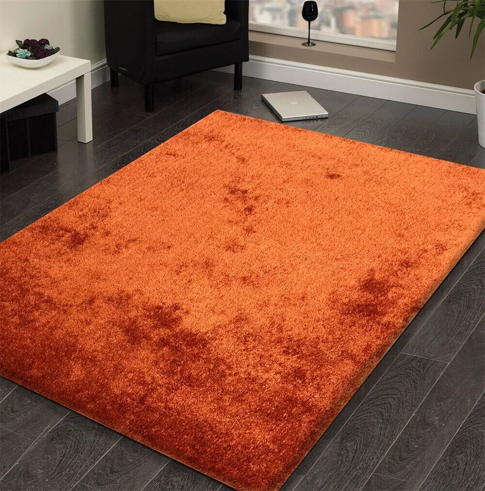 A soft shaggy rust-colored area rug, hand tufted with a cotton backing, displayed in a cozy living room setting.