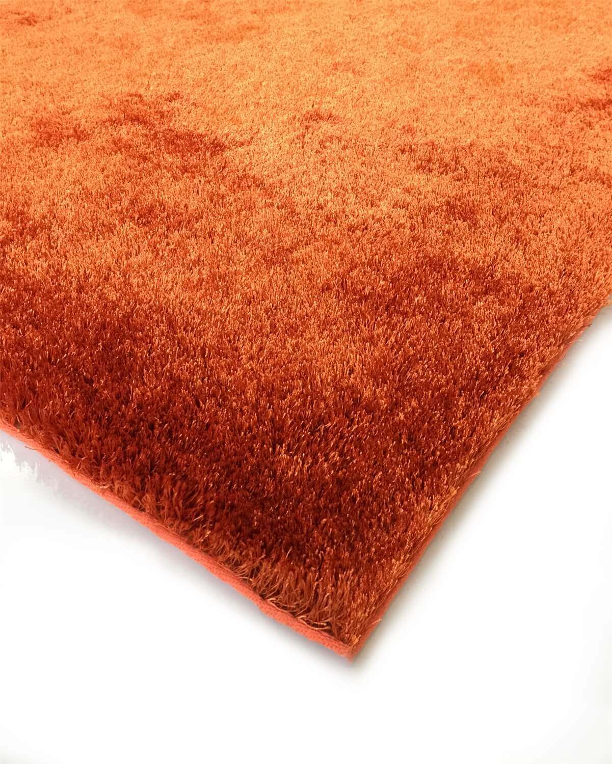 A soft shaggy rust-colored area rug, hand tufted with a cotton backing, displayed in a cozy living room setting.