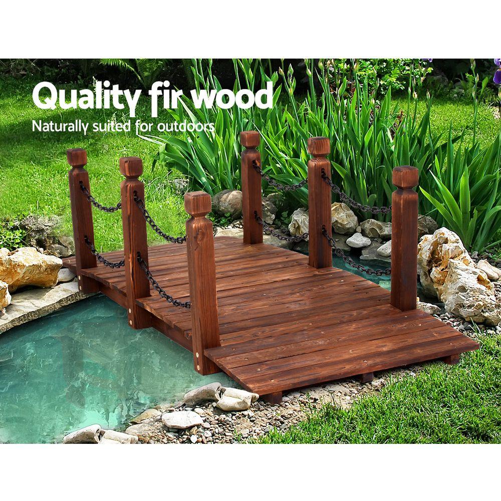 A rustic wooden garden bridge made of burnt fir wood, featuring an arch design with rustic chains and side railings, set in a lush garden landscape.