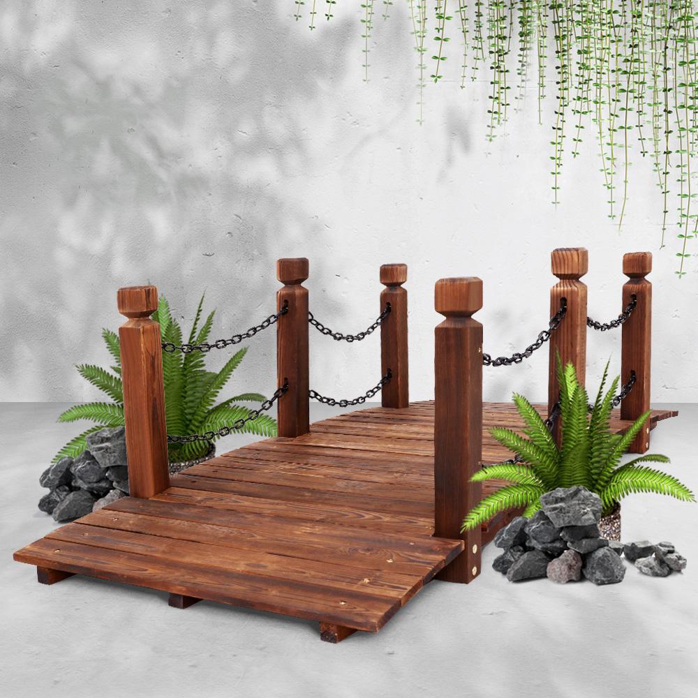 A rustic wooden garden bridge made of burnt fir wood, featuring an arch design with rustic chains and side railings, set in a lush garden landscape.