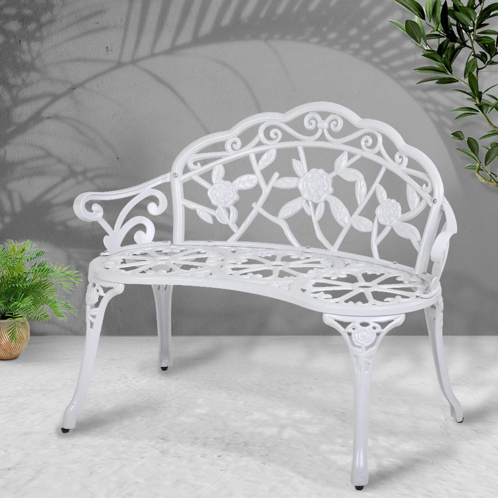 Gardeon Victorian Garden Bench in white with ornate aluminum seat and floral-patterned backrest, set against a garden backdrop.