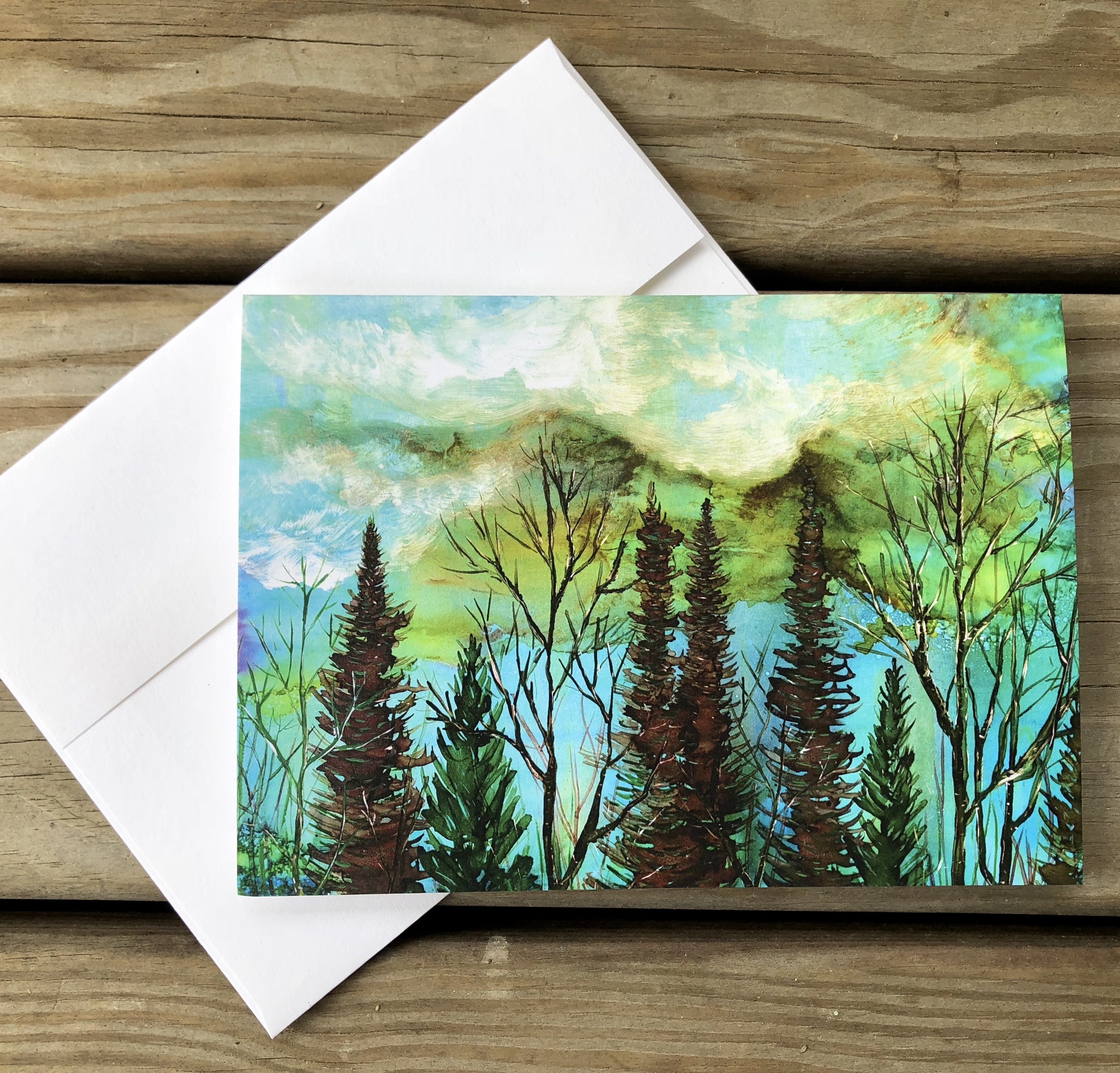 A beautiful greeting card featuring a moody landscape with a vibrant green sky and a tranquil forest below, perfect for gifting or framing.