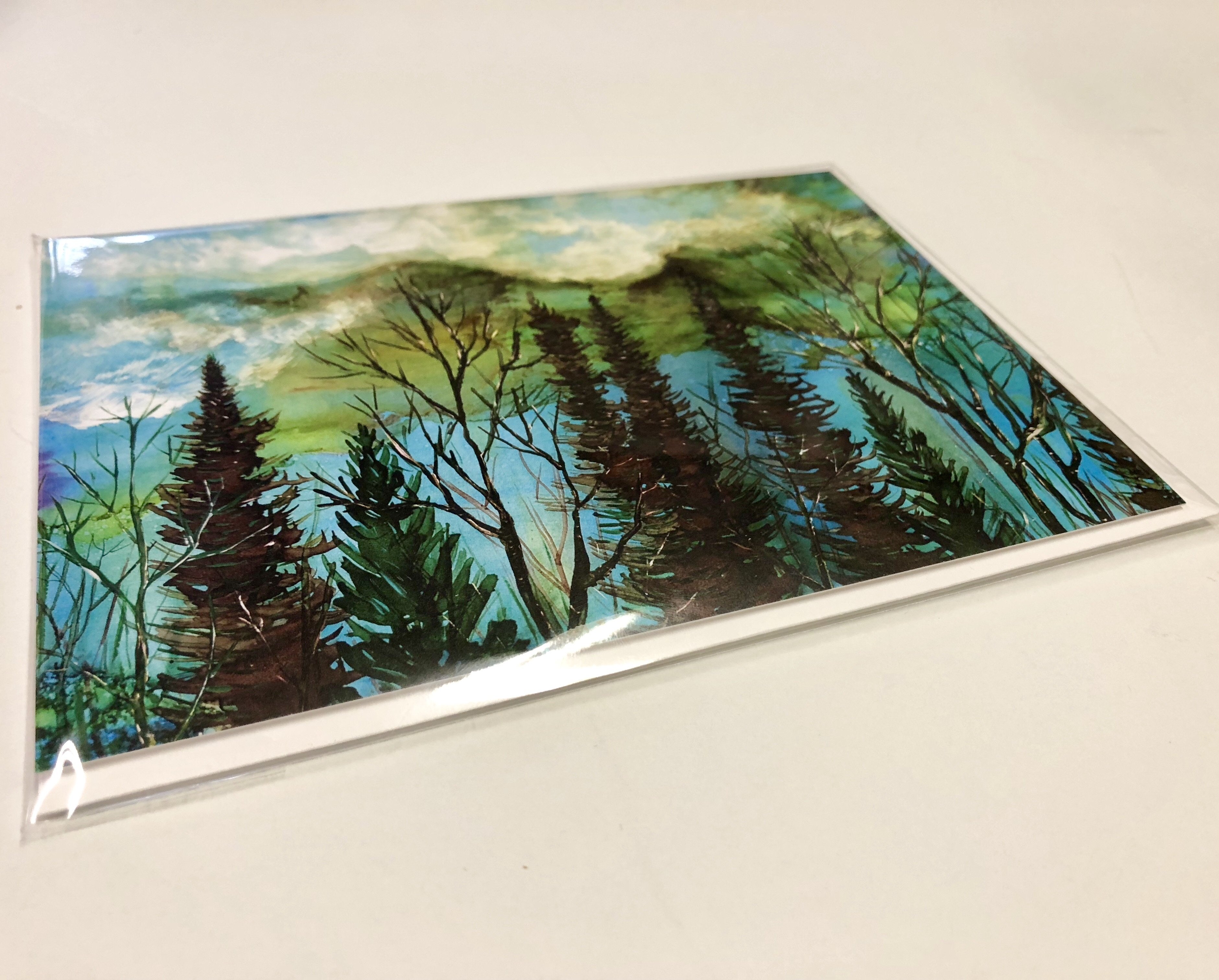 A beautiful greeting card featuring a moody landscape with a vibrant green sky and a tranquil forest below, perfect for gifting or framing.