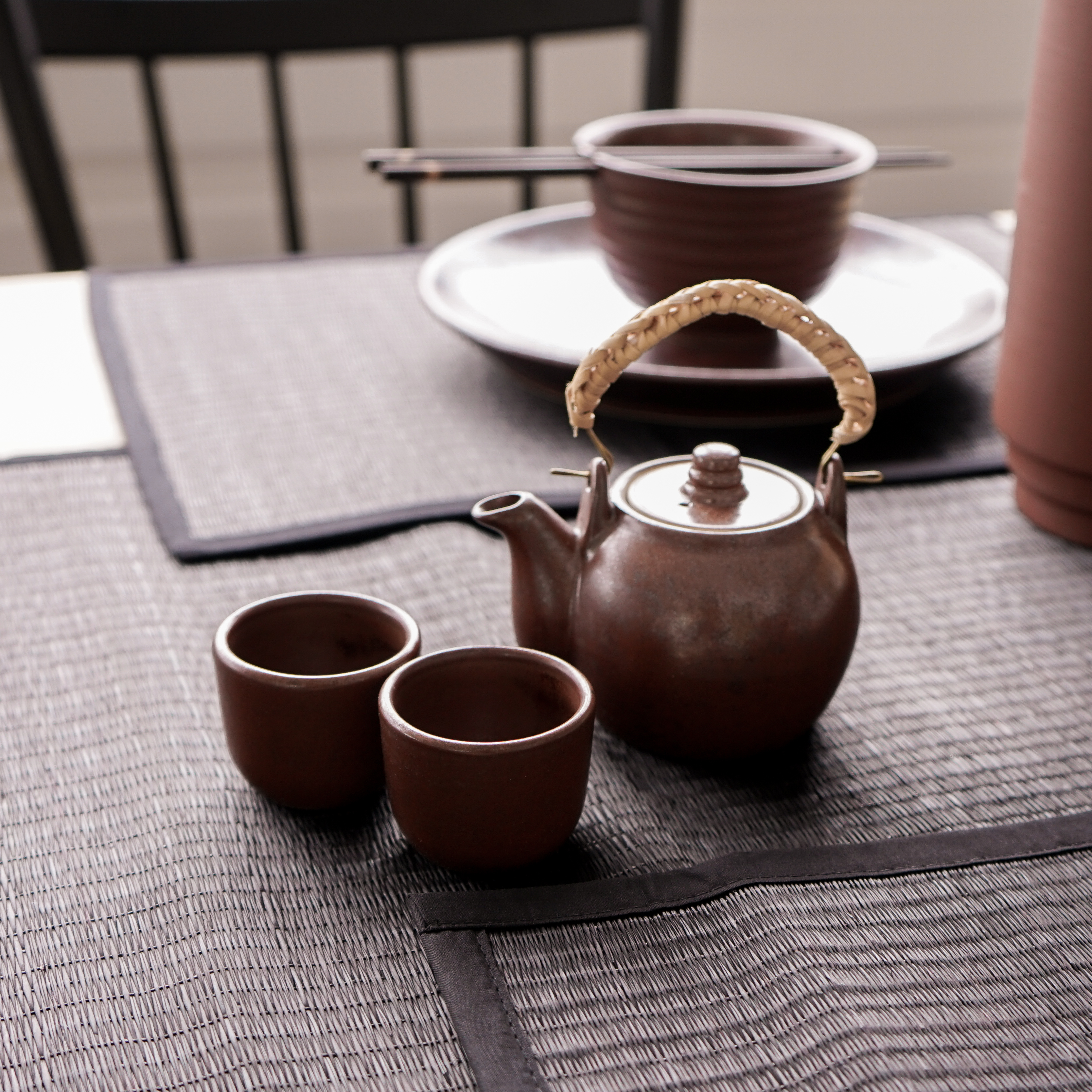 Handmade Chinese teapot set featuring a rustic design with two matching cups and a woven rattan handle.