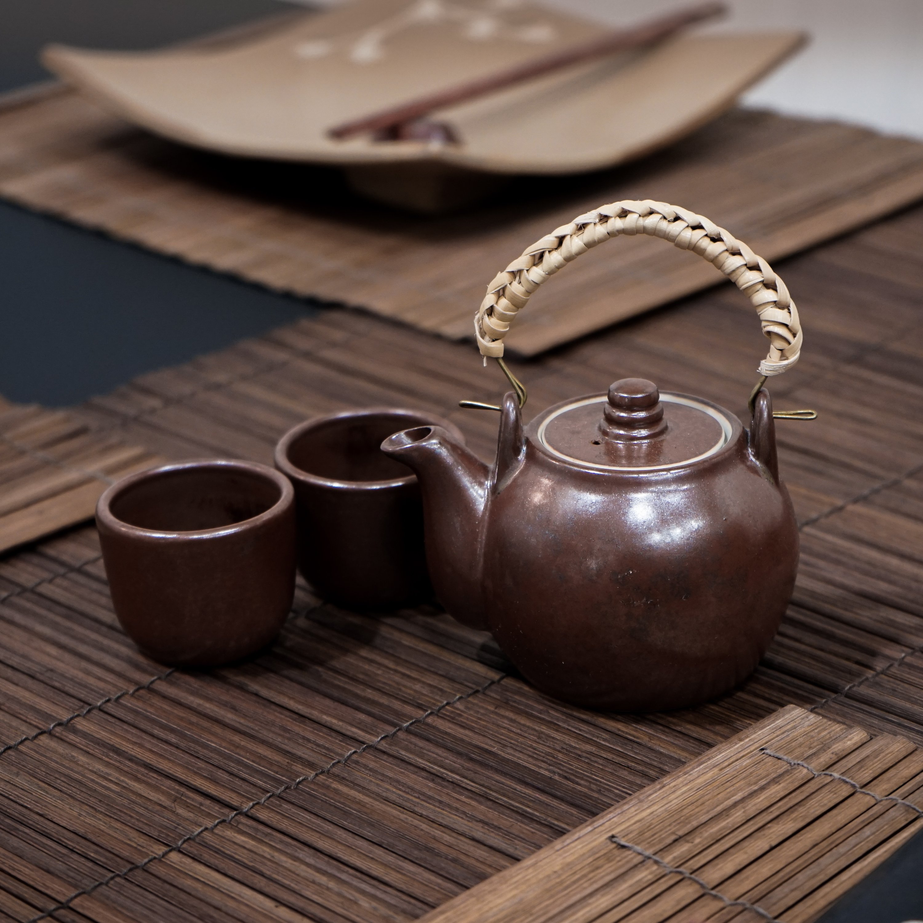 Handmade Chinese teapot set featuring a rustic design with two matching cups and a woven rattan handle.