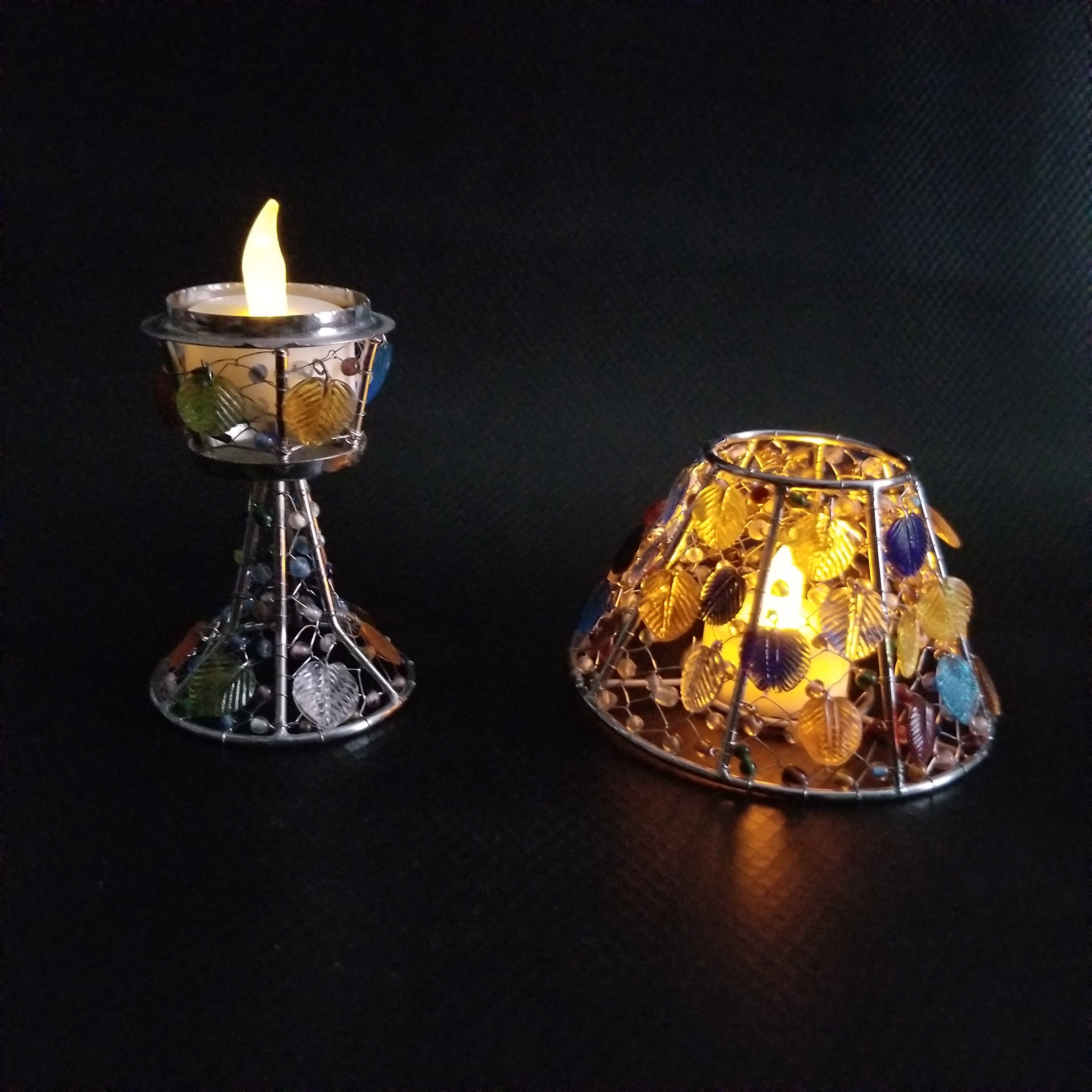 A beautifully handcrafted colored glass tea light candle holder featuring floral motifs and a sturdy spindle, radiating warm candlelight.