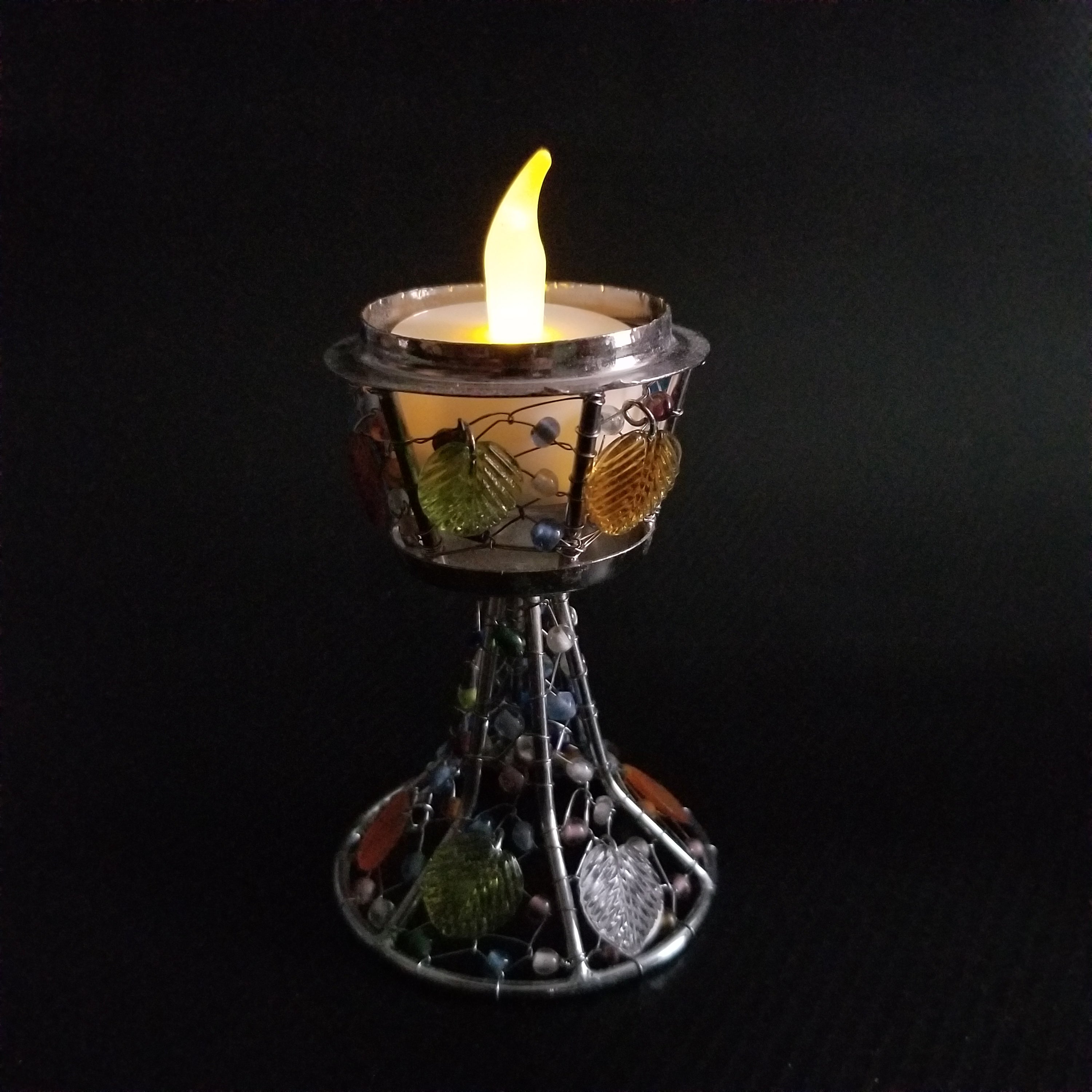 A beautifully handcrafted colored glass tea light candle holder featuring floral motifs and a sturdy spindle, radiating warm candlelight.