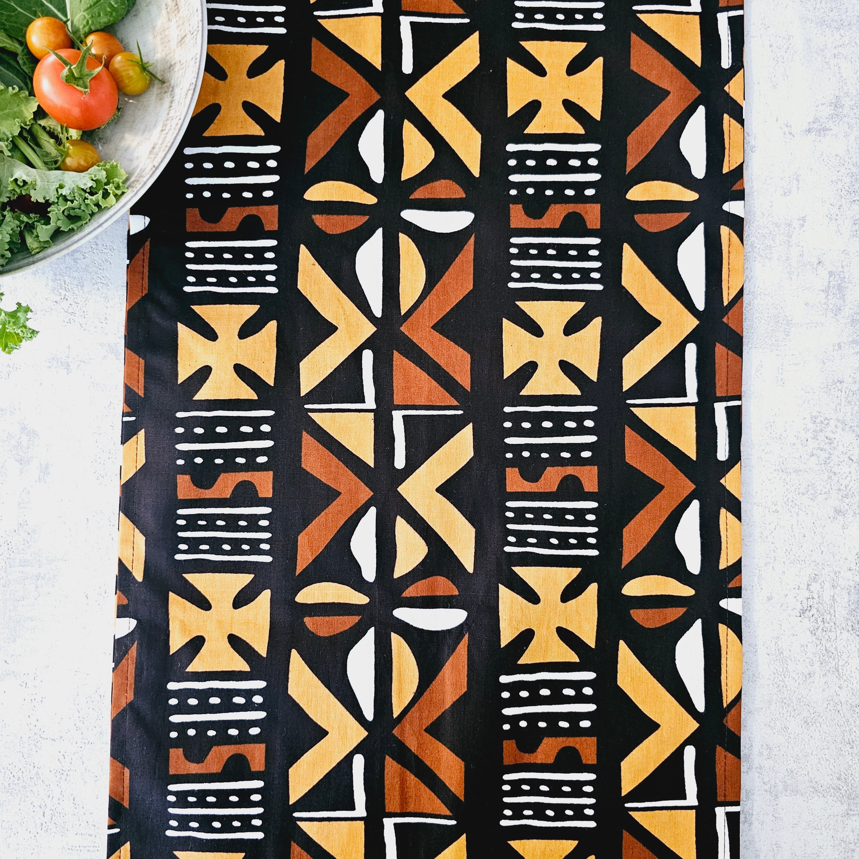 Handmade table runner featuring vibrant African prints, available in three sizes, elegantly draped over a dining table.