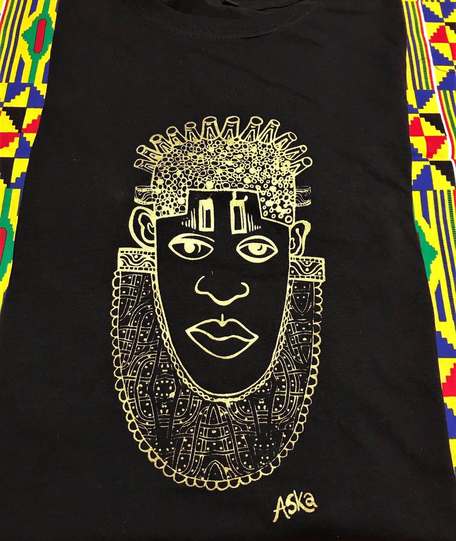 IDIA in Gold Art Earth Positive Tee featuring a gold print of Queen Idia on a black scooped neck shirt made from 100% organic cotton.