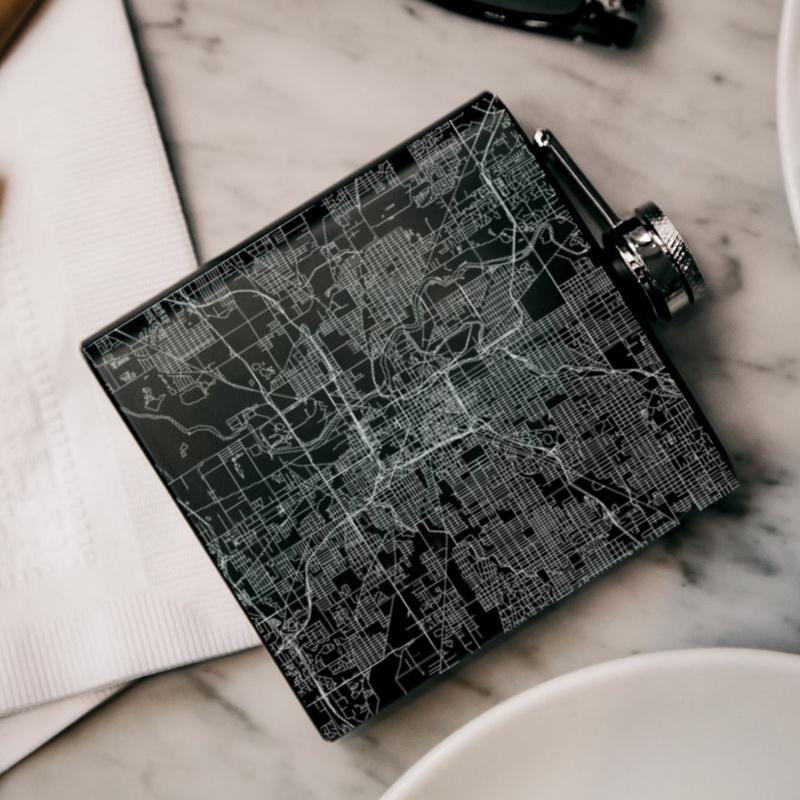 Matte black hip flask featuring a custom engraved map of Indianapolis, Indiana, with coordinates, accompanied by a canvas bag and funnel.