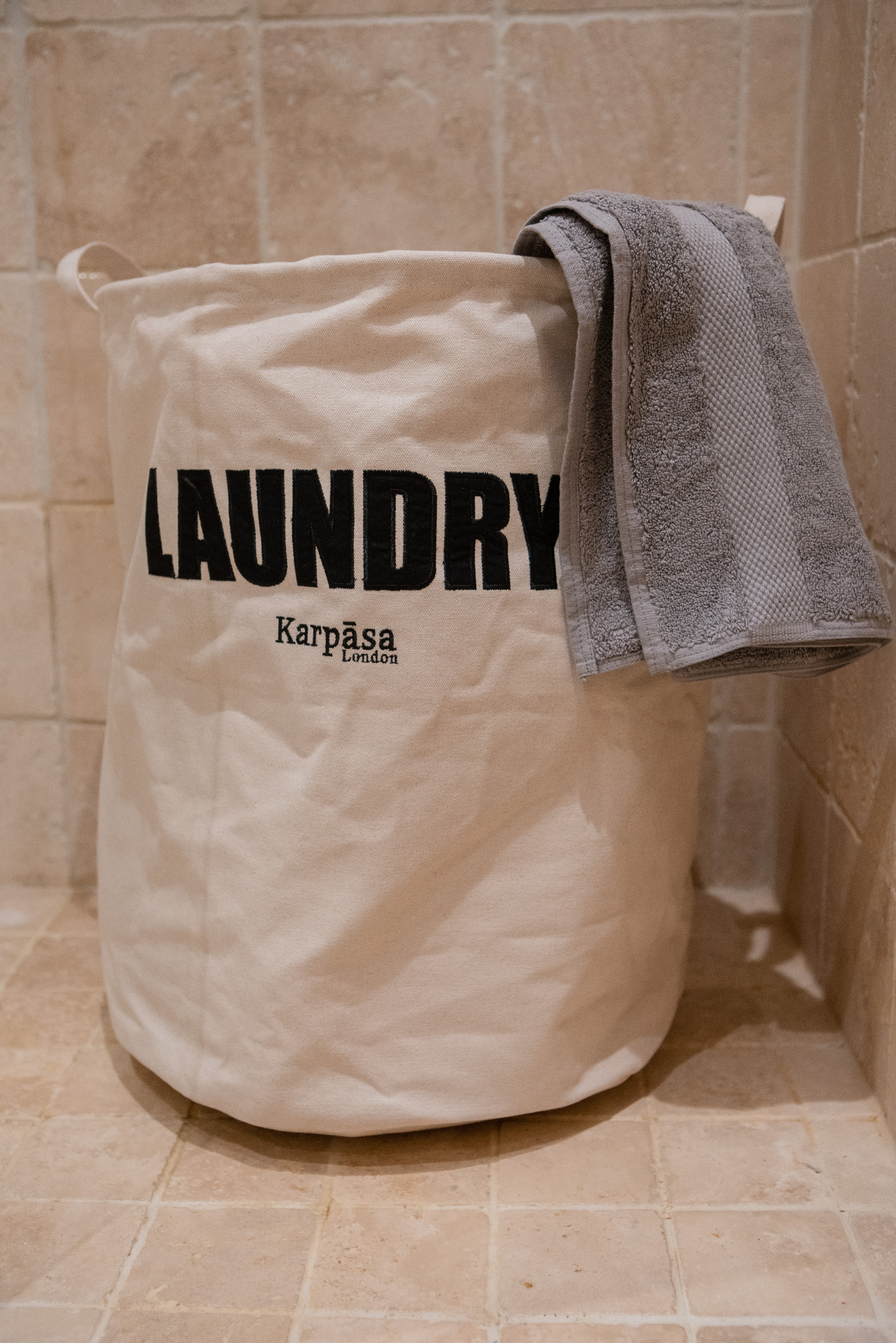 A spacious organic cotton laundry bag with a natural color, featuring a lightweight aluminum ring for stability, perfect for laundry and travel.