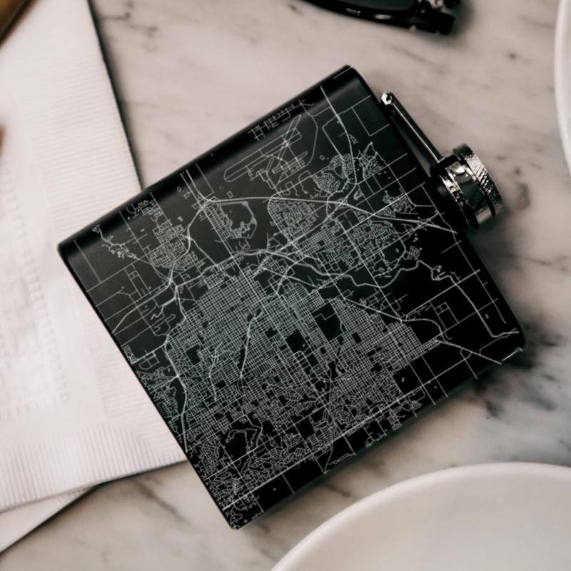 Custom engraved matte black hip flask featuring a map of Lincoln, Nebraska with coordinates, accompanied by a canvas bag and funnel.