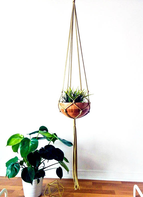 A stylish macrame plant hanger made of gold nylon cord, showcasing a beautiful plant pot, perfect for indoor and outdoor decor.