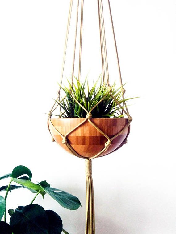 A stylish macrame plant hanger made of gold nylon cord, showcasing a beautiful plant pot, perfect for indoor and outdoor decor.