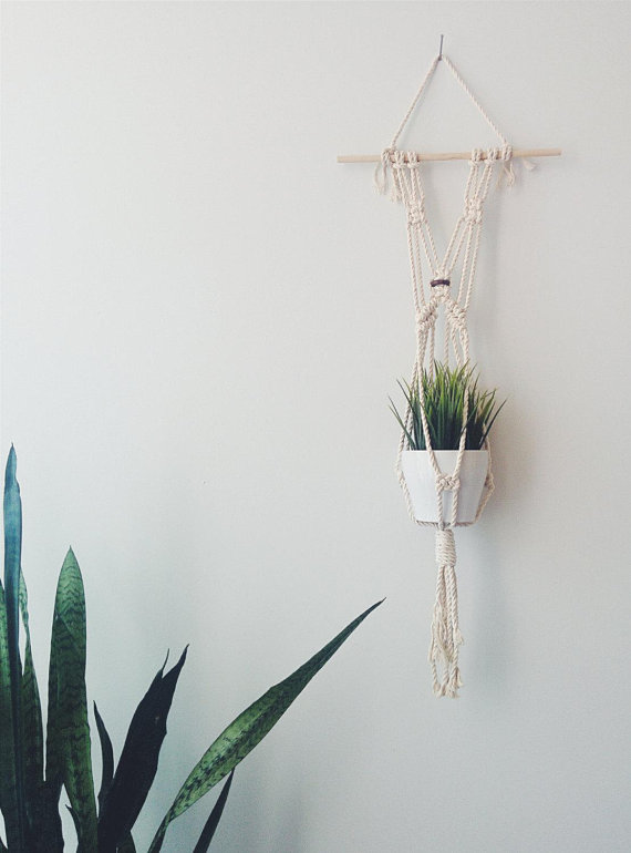 A beautifully crafted handmade macrame plant hanger made from natural cotton rope, featuring a wooden dowel and tassels, designed to hold small plant pots.