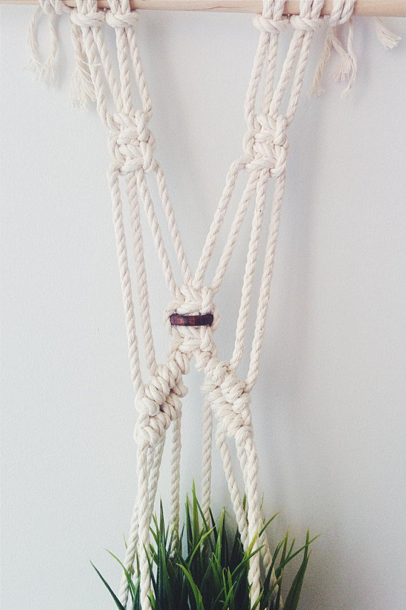 A beautifully crafted handmade macrame plant hanger made from natural cotton rope, featuring a wooden dowel and tassels, designed to hold small plant pots.