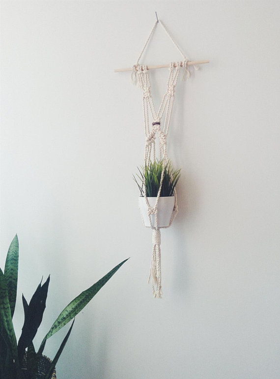 A beautifully crafted handmade macrame plant hanger made from natural cotton rope, featuring a wooden dowel and tassels, designed to hold small plant pots.