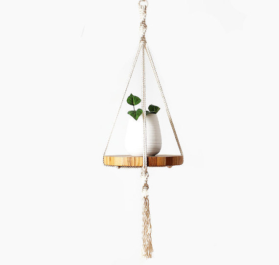 A stylish macrame plant hanger made of 100% ecru cotton, featuring intricate knots and tassels, designed to hold potted plants indoors.