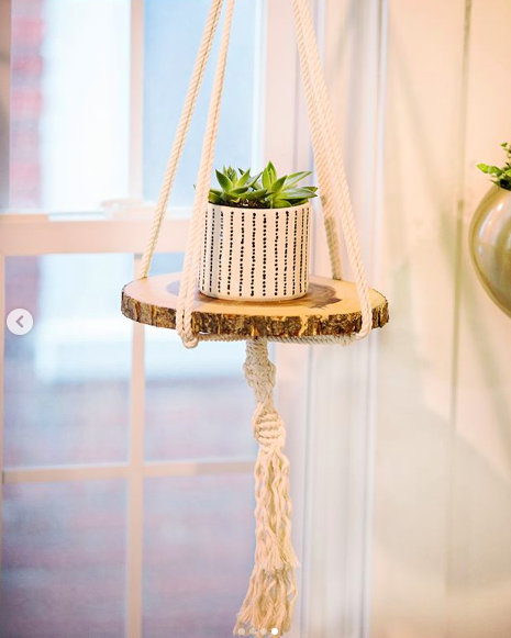 A stylish macrame plant hanger made of 100% ecru cotton, featuring intricate knots and tassels, designed to hold potted plants indoors.