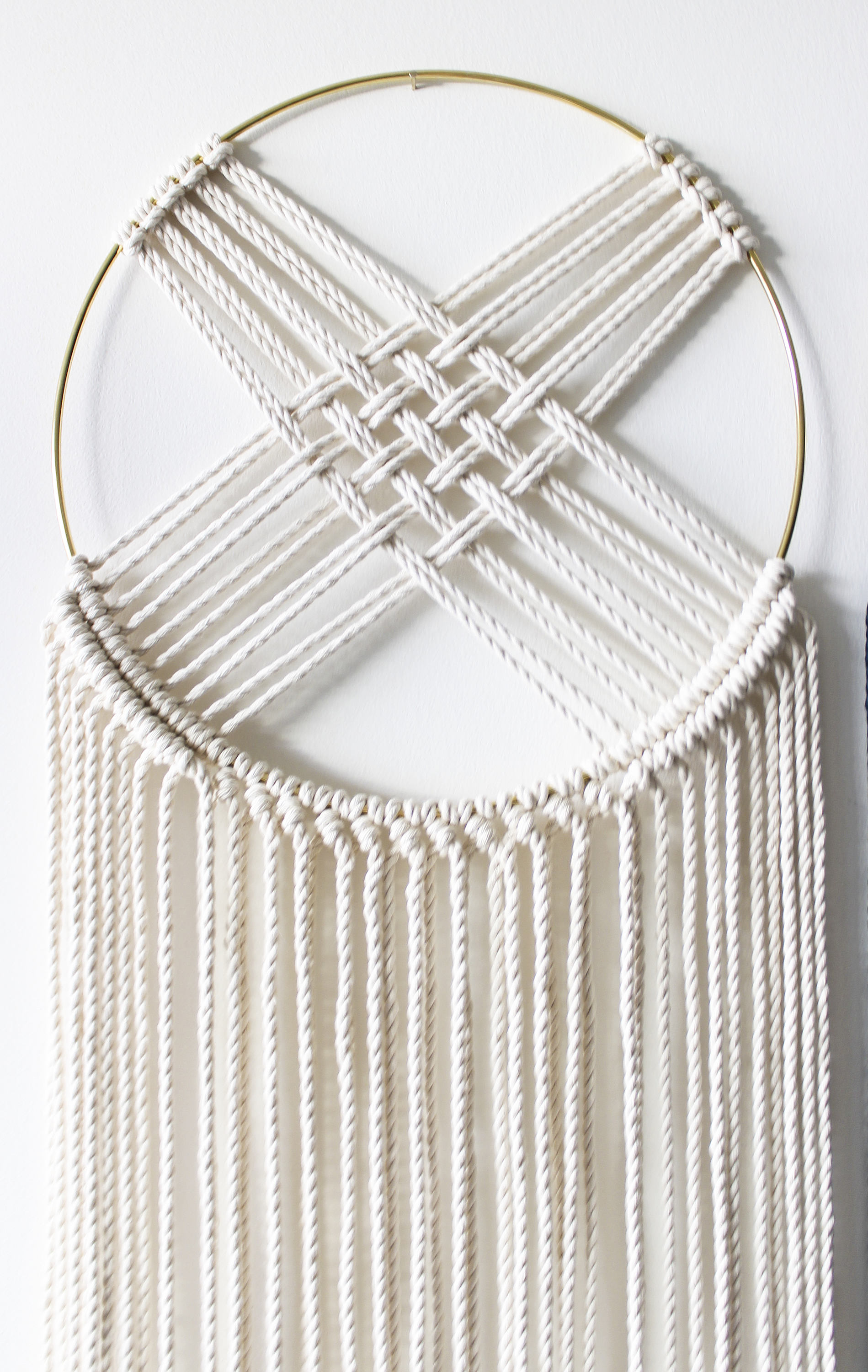 Handcrafted macrame wall hanging featuring a gold metal hoop and intricate cotton rope design, perfect for home or office decor.