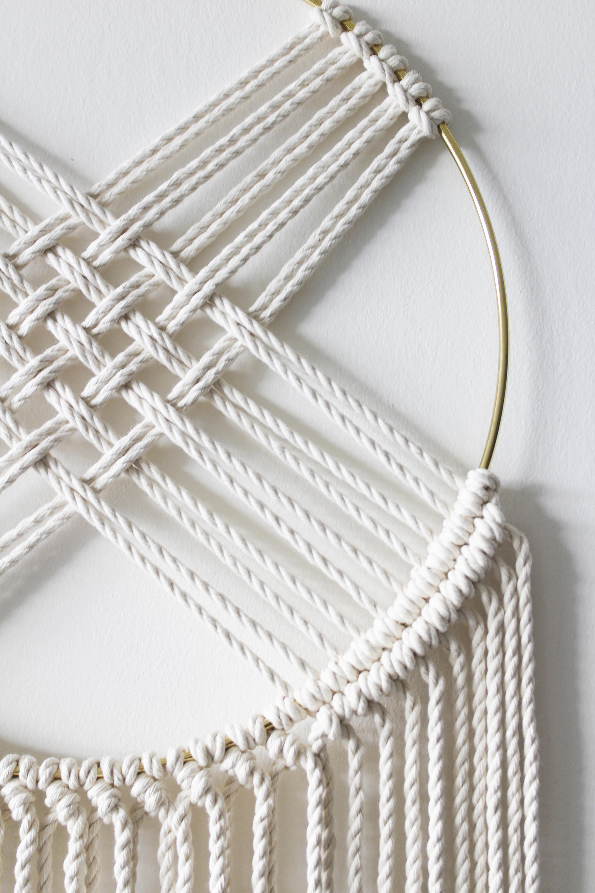 Handcrafted macrame wall hanging featuring a gold metal hoop and intricate cotton rope design, perfect for home or office decor.