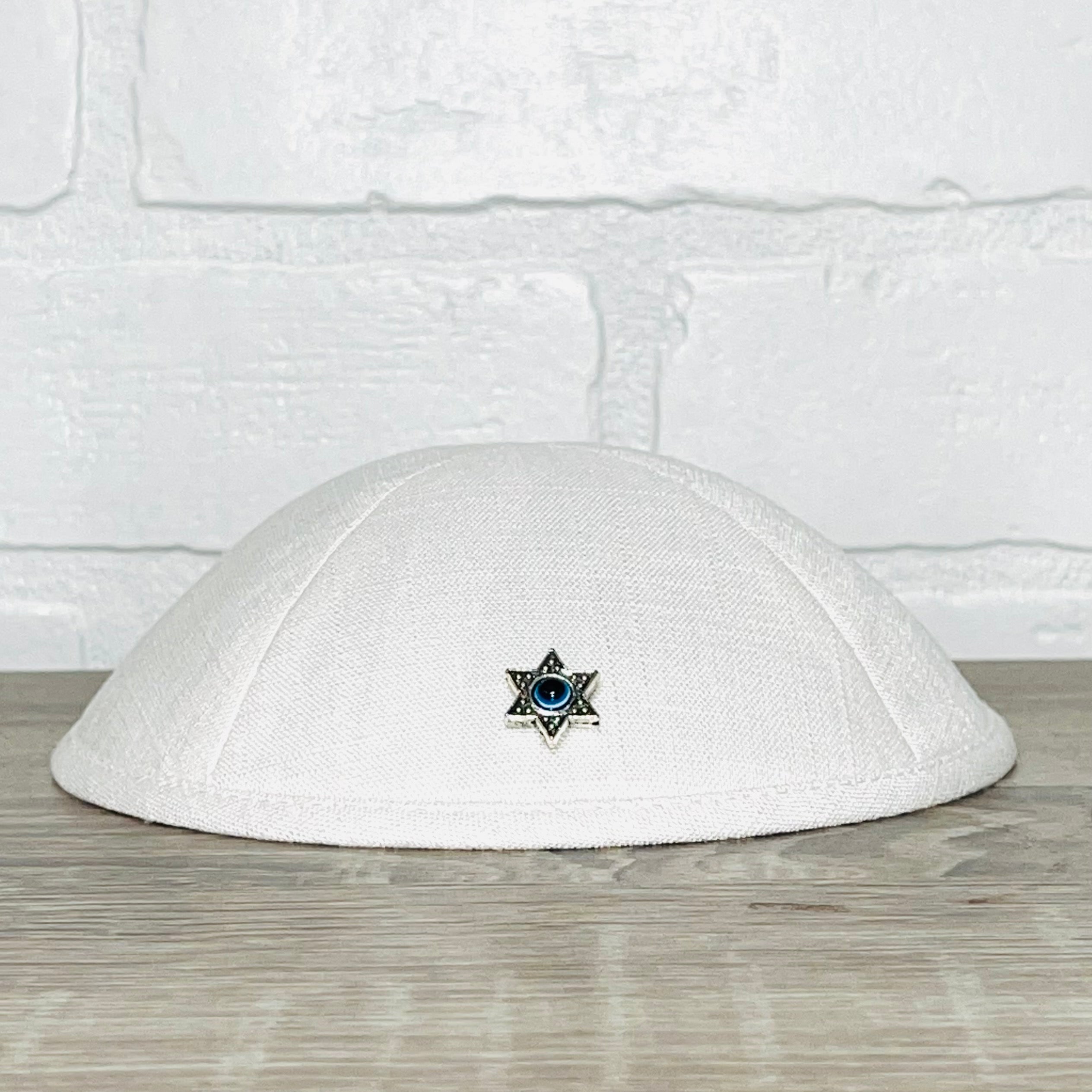 A beautifully crafted Magen David Kippah featuring a blue Evil Eye, available in black cotton, denim, and white linen.