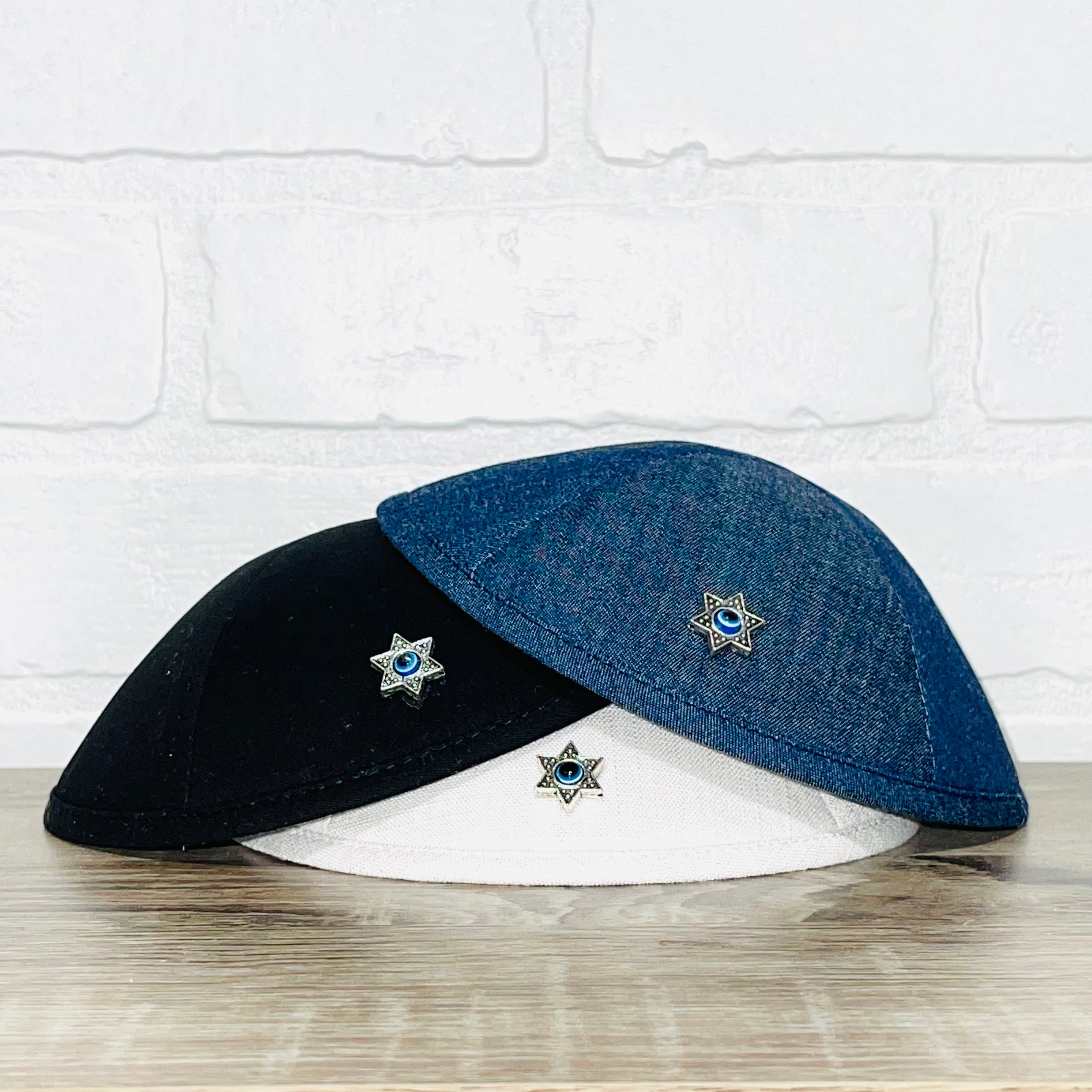 A beautifully crafted Magen David Kippah featuring a blue Evil Eye, available in black cotton, denim, and white linen.